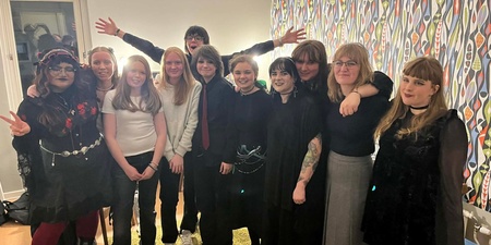 En grupp ungdomar poserar tillsammans inomhus, många klädda i svarta kläder och alternativa stilar.