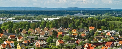 Färgglada villor med röda och gula tak i ett lummigt bostadsområde, omgivna av skog och berg i bakgrunden.