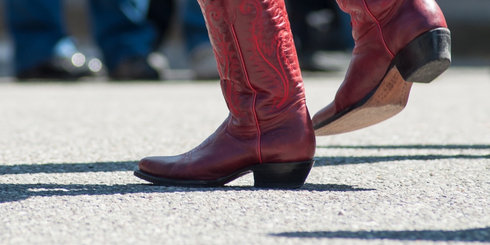 Person i blå jeans och röda cowboyboots dansar utomhus på asfalt.