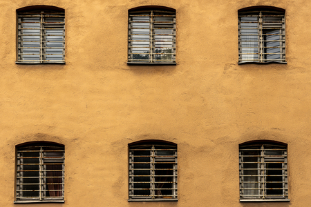 Sex fönster med galler på en gul putsad vägg, ordnade i två rader om tre.