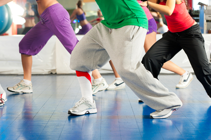 Flera personer tränar tillsammans i ett gym, klädda i färgglada träningskläder och sneakers.