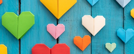 Flera färgglada origamihjärtan i olika storlekar på en blå träbakgrund.