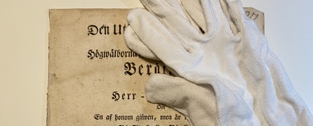Ett gammalt svenskt dokument från 1768 med vita handskar ovanpå, liggande på ett bord.