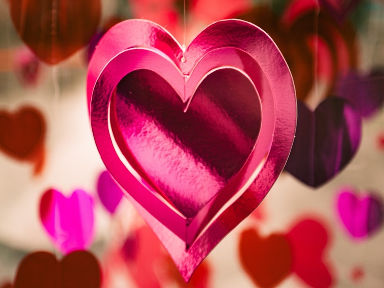 Flera rosa och röda hjärtan hänger i luften, med ett stort glansigt hjärta i fokus.