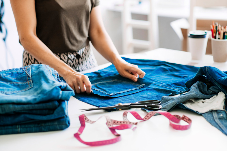 Person arbetar med att sy om jeans på ett bord med sax, måttband och andra syverktyg.