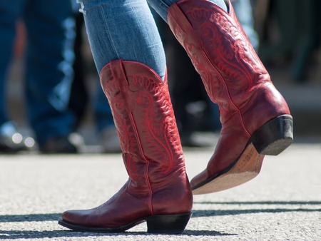 Person i blå jeans och röda cowboyboots dansar utomhus på asfalt.