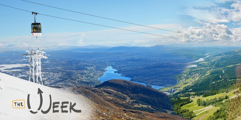 Landskapsbild med linbana över fjäll, sjö och grönskande dal under blå himmel.