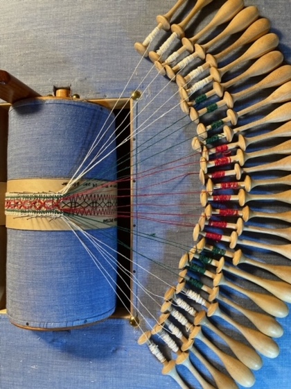 En närbild av en spetsklubb med många trådar och träspolar, används för att tillverka spets.