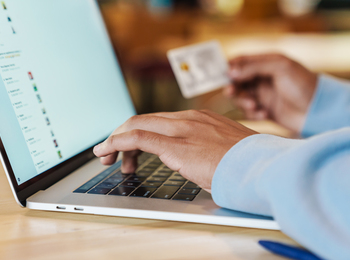 En person använder en bärbar dator och håller ett kreditkort, troligen för onlineköp.