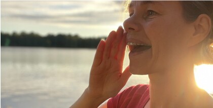 Person står vid en sjö i solnedgång och håller handen vid munnen som om de ropar.