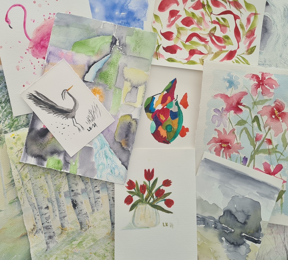 Flera akvarellmålningar med blommor, fåglar och naturmotiv ligger utspridda på ett bord.