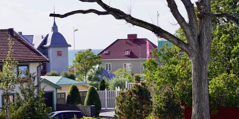Vy över ett bostadsområde med färgglada hus, trädgårdar och ett stort träd i förgrunden.