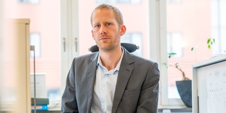 Linus Olofsson sitter på en kontorsstol i ett ljust kontorsrum med stora fönster.