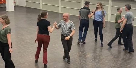 Sex personer dansar pardans i en ljus sal med trägolv.