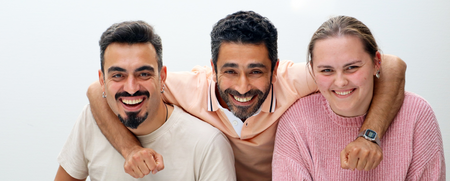 Tre personer sitter tillsammans och ler mot kameran, en man i mitten har armen runt de andra två.