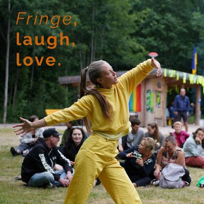 En kvinna i gula kläder dansar utomhus inför en sittande publik. Texten 'Fringe, laugh, love.' syns i bilden.
