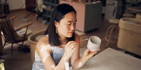 En kvinna målar en keramikmugg med pensel i en ljus keramikstudio.