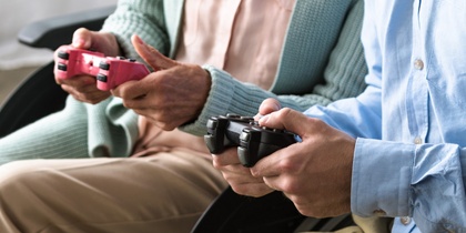 En äldre kvinna i rullstol och en yngre man spelar tv-spel tillsammans i ett ljust vardagsrum.