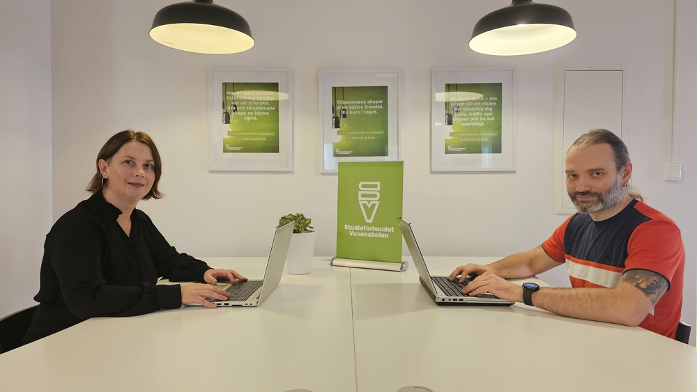 Två personer sitter mittemot varandra vid ett vitt bord med laptops i ett modernt kontor.