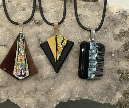 Tre geometriska hängsmycken i glas med färgglada mönster ligger på en kristallsten.