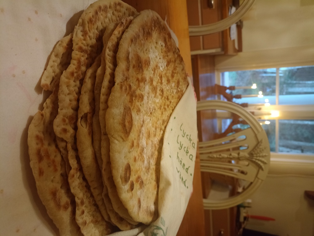 En stapel hembakat tunnbröd på ett bord i ett hemtrevligt kök med tända ljus i bakgrunden.