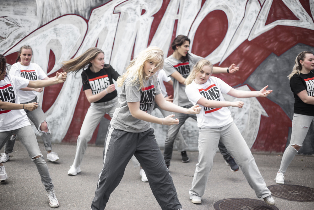 En grupp unga personer dansar hiphop utomhus framför en graffitivägg.