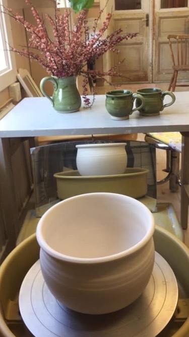 En keramikverkstad med drejskiva, en ofärgad skål och gröna keramikkannor på ett bord.