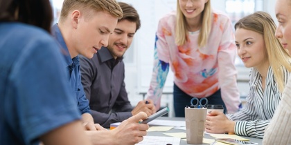 En grupp unga vuxna sitter runt ett bord och diskuterar dokument och en surfplatta.