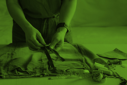 Person syr eller lagar ett plagg med dragkedja, omgiven av sytråd och måttband på ett bord.