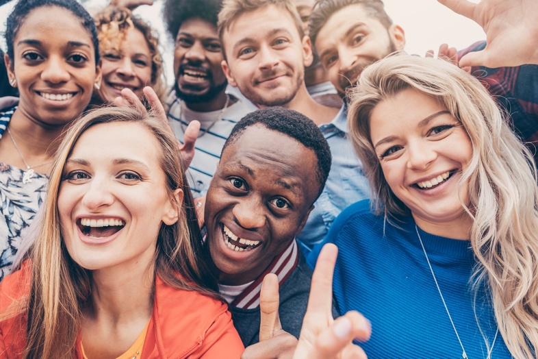 En grupp glada unga vuxna står tätt tillsammans och ler mot kameran utomhus.