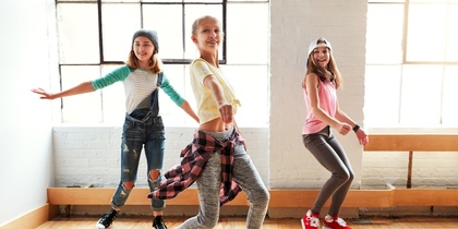 Tre unga personer dansar i ett ljust rum med stora fönster och trägolv.