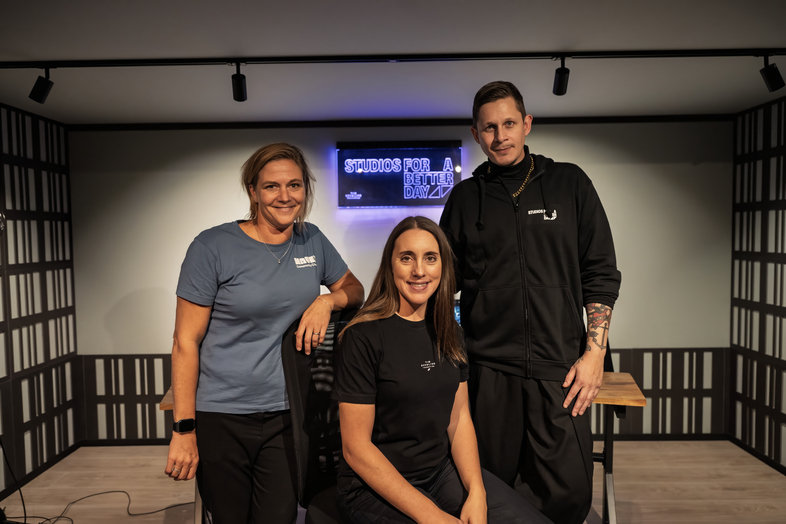 Tre personer poserar i en modern studio med en skylt som lyser i bakgrunden.