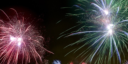 Färgglada fyrverkerier lyser upp natthimlen över ett bostadsområde med flerfamiljshus.