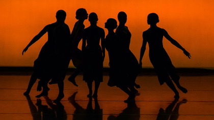 Sex dansare i silhuett mot en orange bakgrund, poserar tillsammans på scenen.