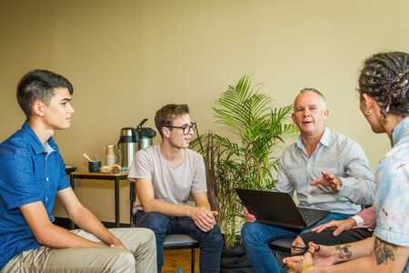 Fyra personer sitter i en ring och diskuterar. En person har en laptop i knät.