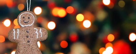 En pepparkaksgubbe hänger i ett snöre framför en suddig bakgrund med färgglada julbelysningar.