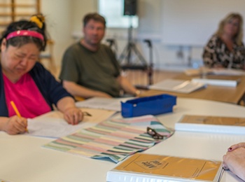 Personer sitter runt ett bord i ett klassrum och arbetar med papper och böcker.