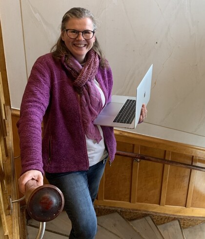 Leende person med glasögon och laptop står i en trappa och håller i ledstången.