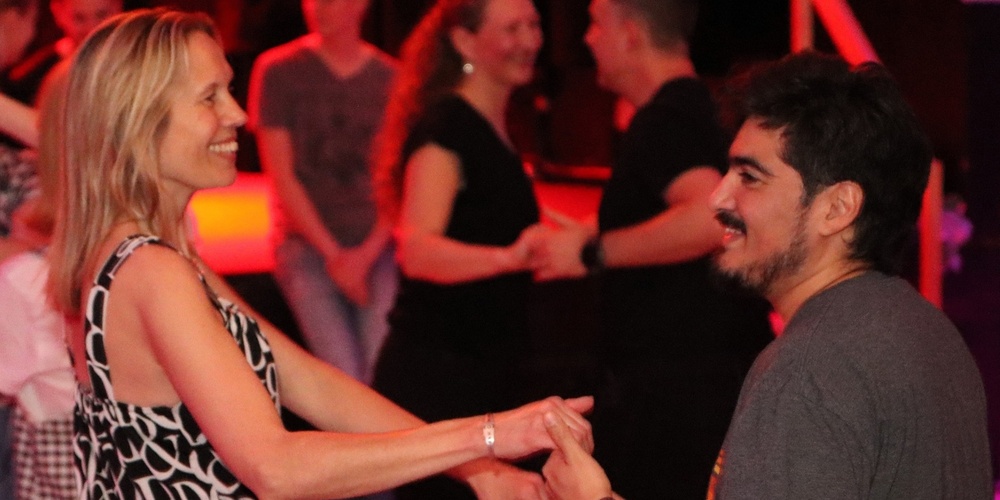 Två personer dansar tillsammans på ett dansgolv med andra par i bakgrunden.