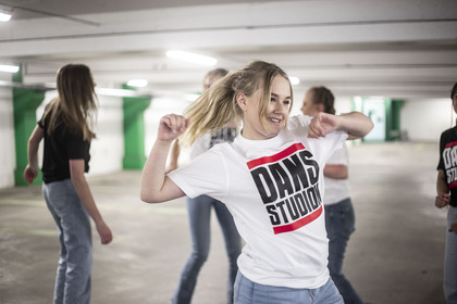 Ung kvinna dansar energiskt i ett parkeringsgarage tillsammans med andra ungdomar.