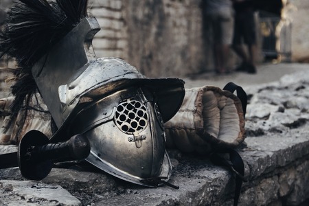 En gammal riddarhjälm och vadderade handskar ligger på en stenmur utomhus.