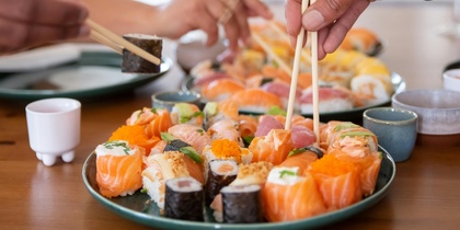 Två personer plockar sushi med ätpinnar från ett fat på ett matbord.
