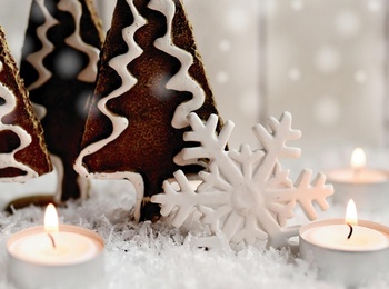 Juldekoration med pepparkaksträd, tända värmeljus, silverkula och snöflinga på konstsnö.