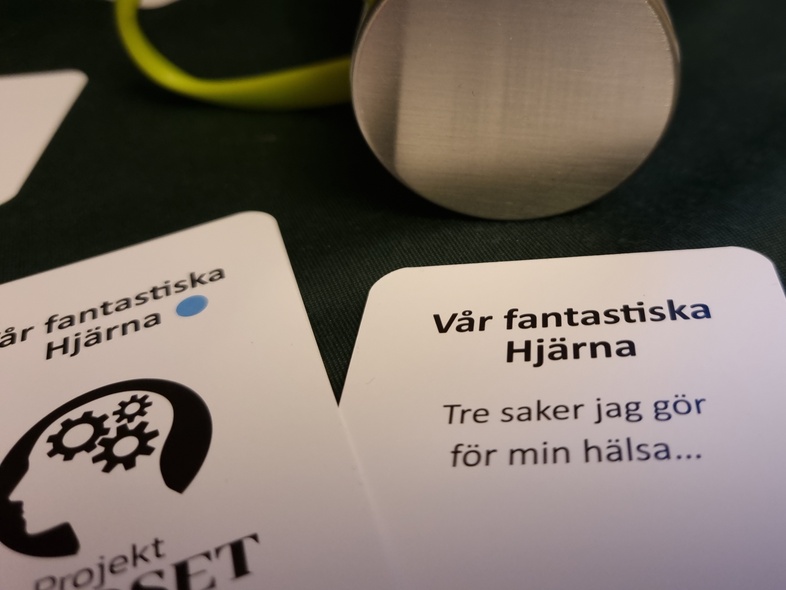 Två kort med text på svenska och en vattenflaska med grön ögla på ett bord.