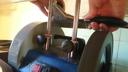 En person slipar en kniv med hjälp av en slipmaskin och ett verktygsfäste.