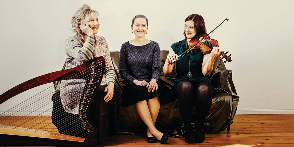 Tre kvinnor sitter på en soffa, en spelar harpa, en fiol och en sitter i mitten utan instrument.
