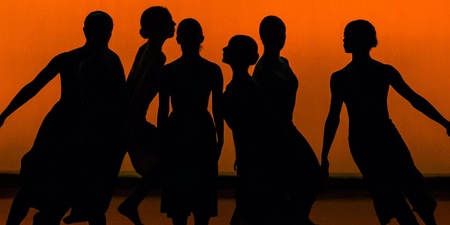 Sex dansare i silhuett poserar mot en orange bakgrund på en scen.