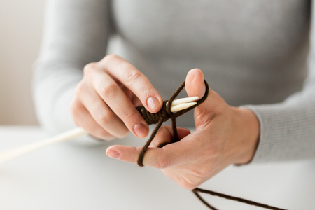 Närbild på händer som stickar med bruna garntrådar och vita stickor.