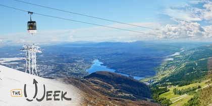 Landskapsvy med linbana över snötäckta och gröna berg, sjö och blå himmel.