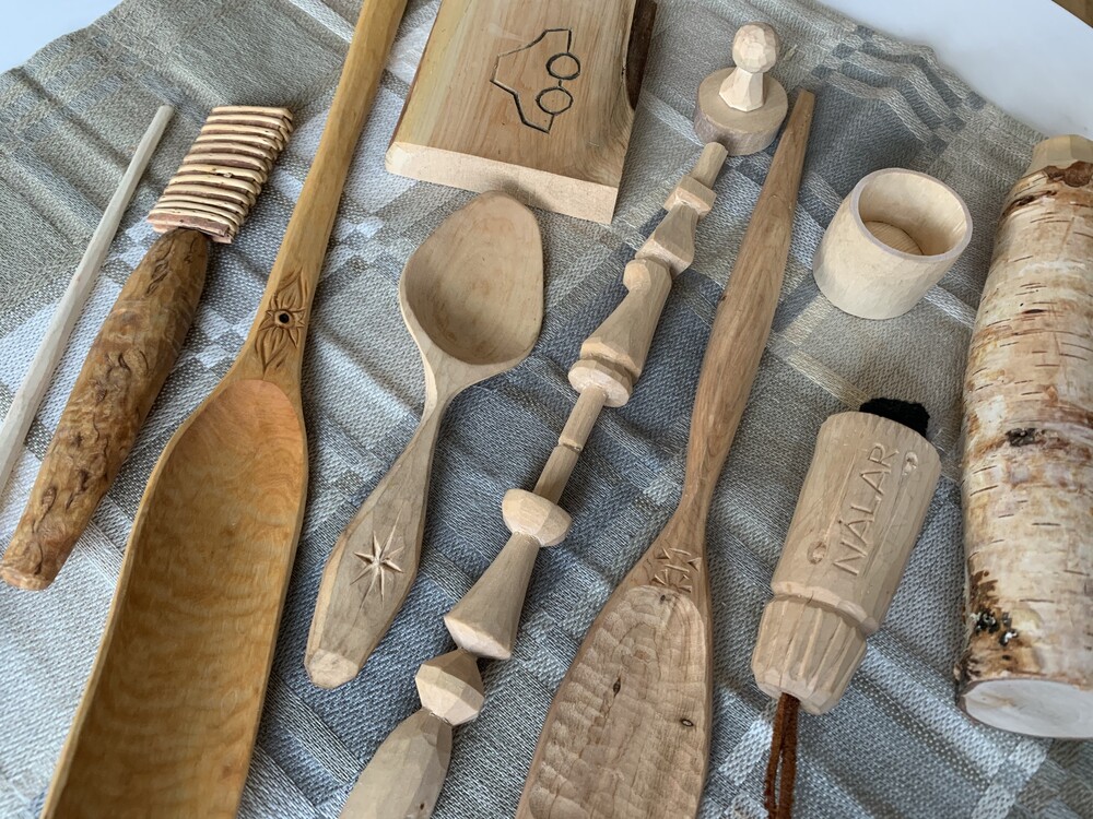 Handgjorda träföremål, som skedar och koppar, ligger på en gråmönstrad duk.